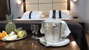 Habitación de hotel con una cama bien hecha, una bandeja de desayuno con frutas y una botella, y un recipiente metálico sobre la mesa.
