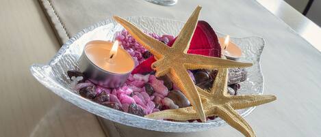 A decorative glass bowl on a table with candles, a starfish, and a red leaf.