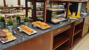 Um balcão de buffet com diversos doces, incluindo croissants e donuts, e uma estação de café com uma máquina de café e sucos.
