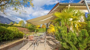 An outdoor patio with a table and chairs, surrounded by greenery and a mountain backdrop. - Comfort Hotel Grenoble Meylan (Meylan)