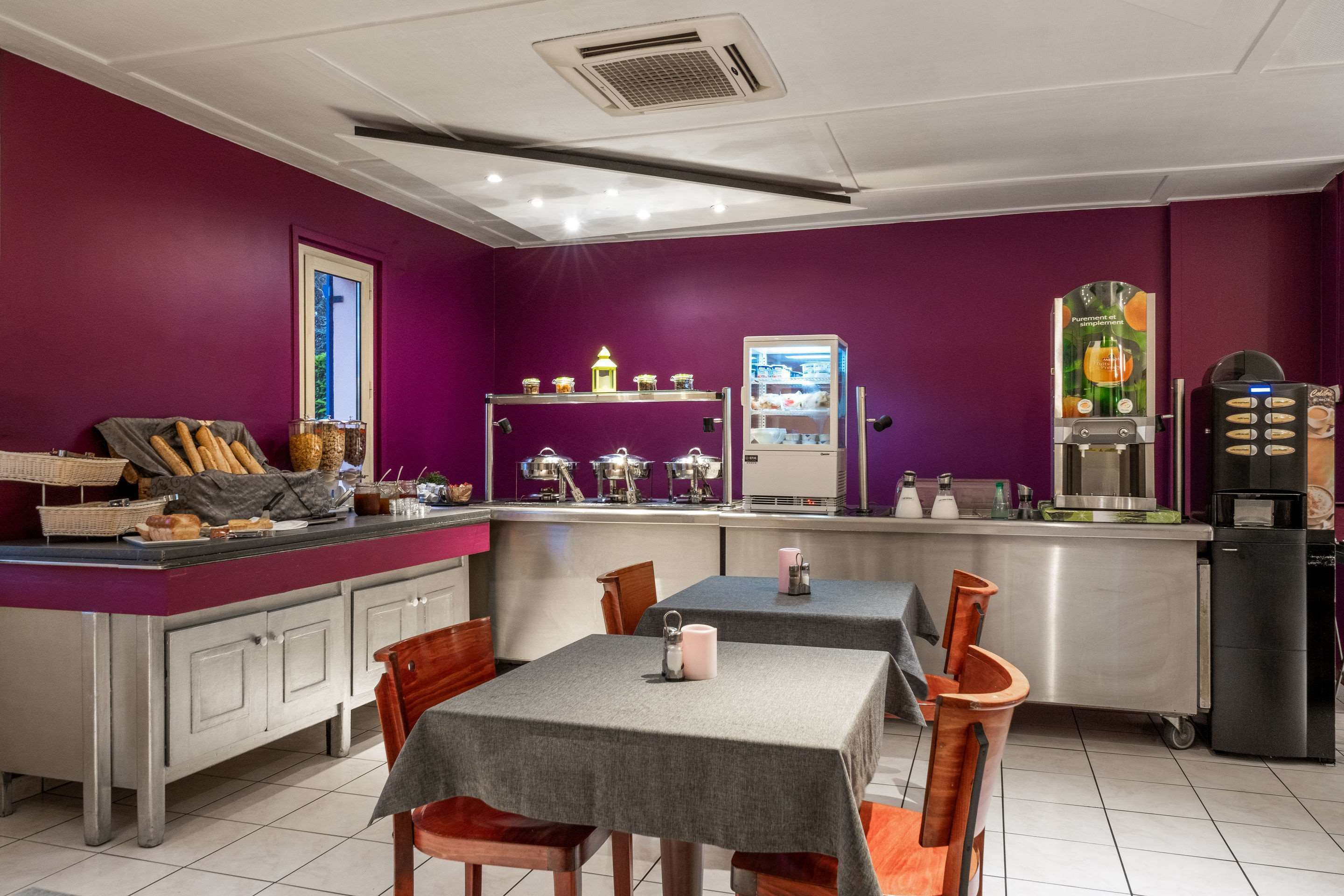 A restaurant with purple walls, a counter with bread and pastries, and tables with chairs.