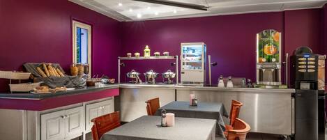 A restaurant with purple walls, a counter with bread and pastries, and tables with chairs.