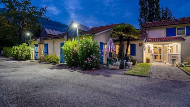 A hotel with a paved driveway, a covered outdoor seating area, and a well-maintained garden with flowering plants. - Comfort Hotel Grenoble Meylan (Meylan)