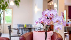 A room with a brown leather sofa, a pink cushion, and a vase of purple orchids. - Comfort Hotel Grenoble Meylan (Meylan)