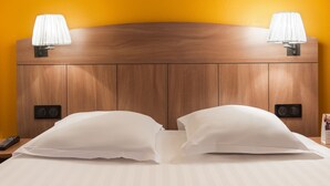 A hotel room with a wooden headboard, two bedside lamps, a remote control, and a bed with white linens. - Comfort Hotel Grenoble Meylan (Meylan)