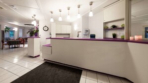 A modern reception area with a white counter, purple accents, and pendant lighting. - Comfort Hotel Grenoble Meylan (Meylan)