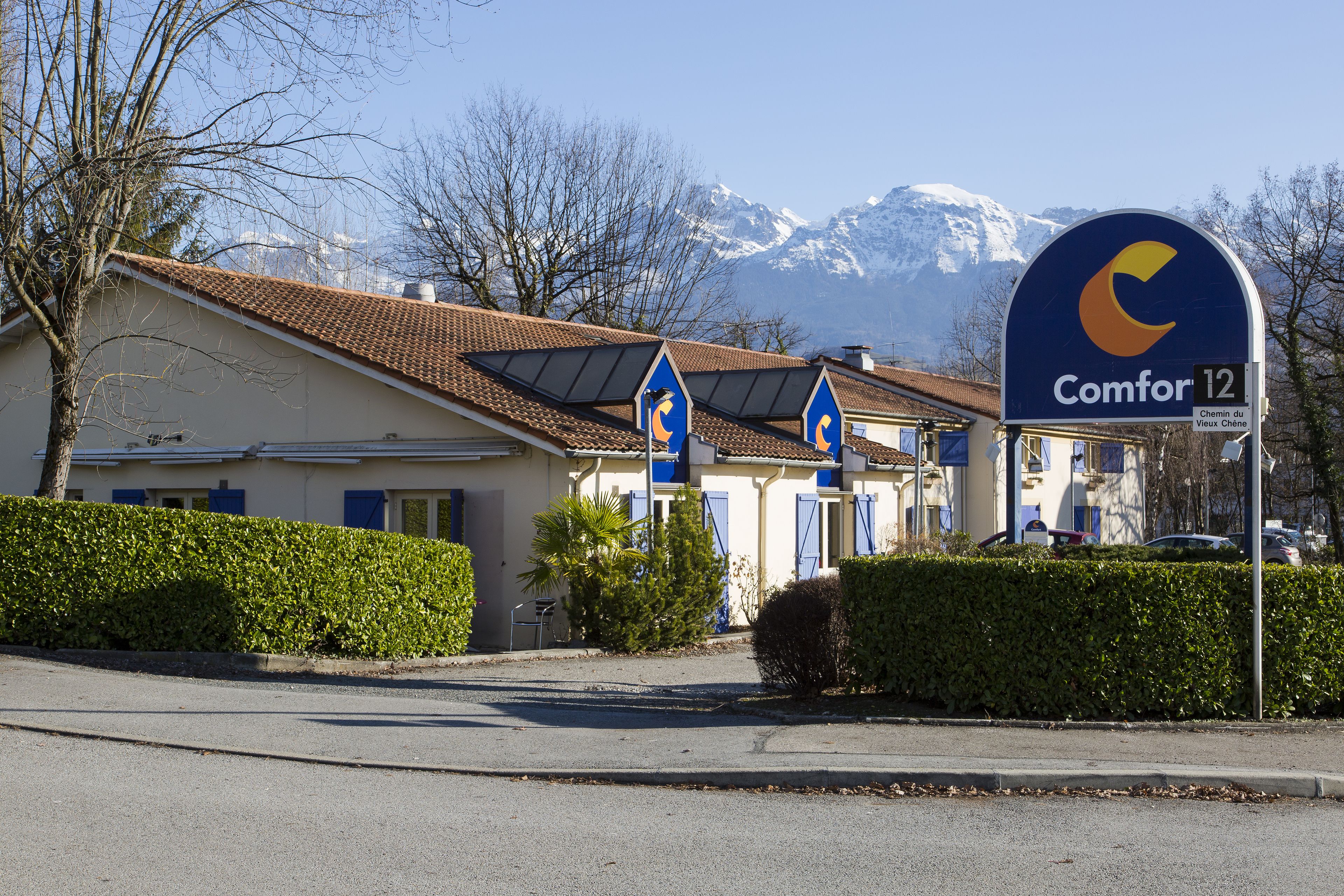 Un hotel con montañas al fondo, paneles solares en el techo y un cartel que indica 'Comfor 12'.