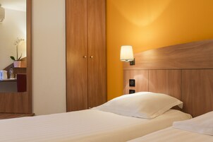 Une chambre d’hôtel avec une tête de lit en bois, une lampe de chevet et un lit recouvert de draps blancs.