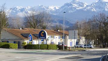 Un hotel con montañas al fondo, un cartel que indica un restaurante y un estacionamiento con coches.
