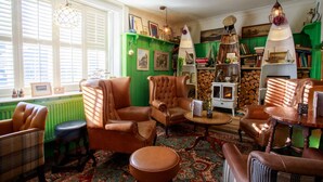 Una sala de estar acogedora con paredes verdes, sillones de cuero, una chimenea y una estantería llena de libros y objetos decorativos.