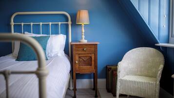 Un dormitorio con cama, una mesita de noche con lámpara, una silla de mimbre y una maleta.