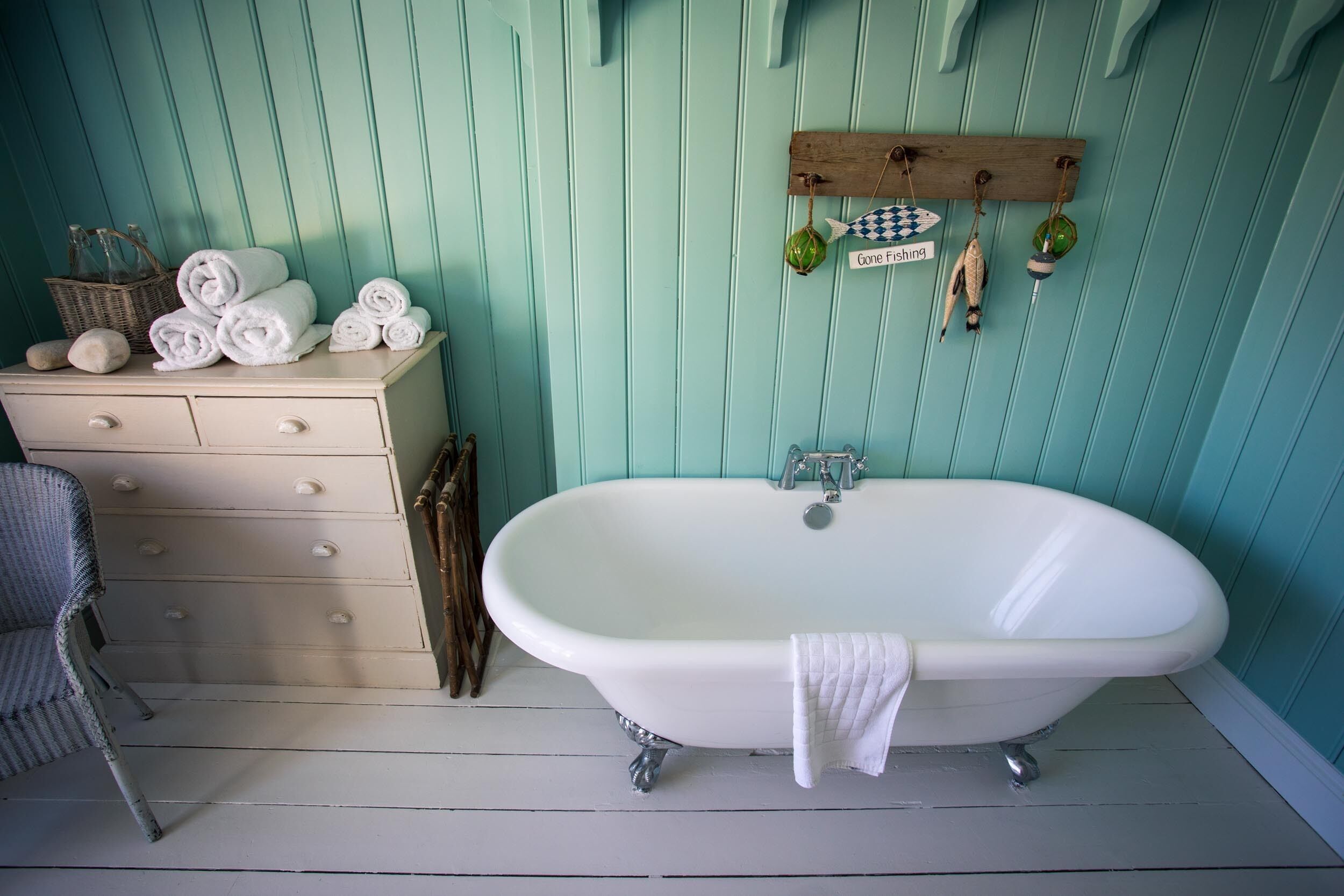 A bathroom with a white clawfoot bathtub, a wooden shelf with fishing lures, and a wicker basket with rolled towels.