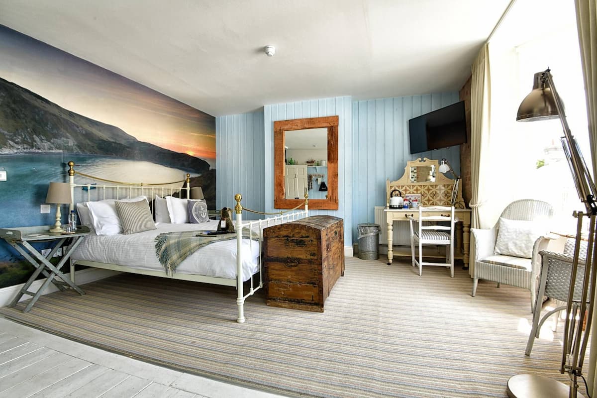 A bedroom with a bed, a wooden chest, a desk, a chair, and a mirror.