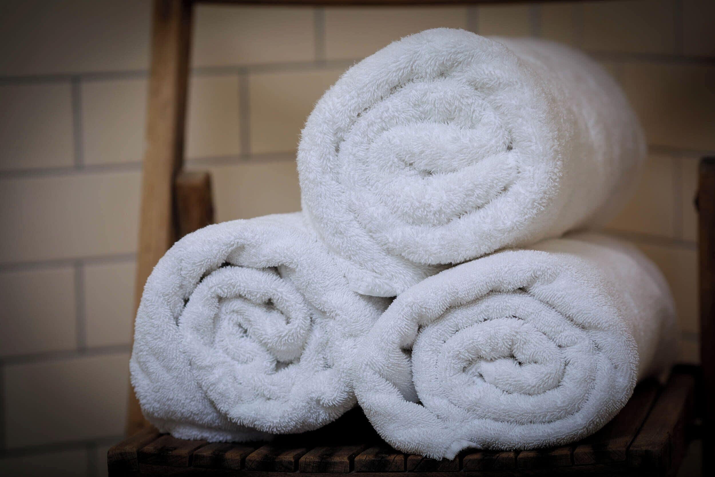 Three neatly rolled white towels stacked on a wooden bench.