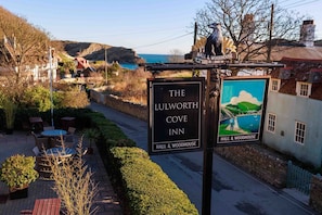 A sign for The Ludworth Cove Inn with a view of the sea and hills in the background.