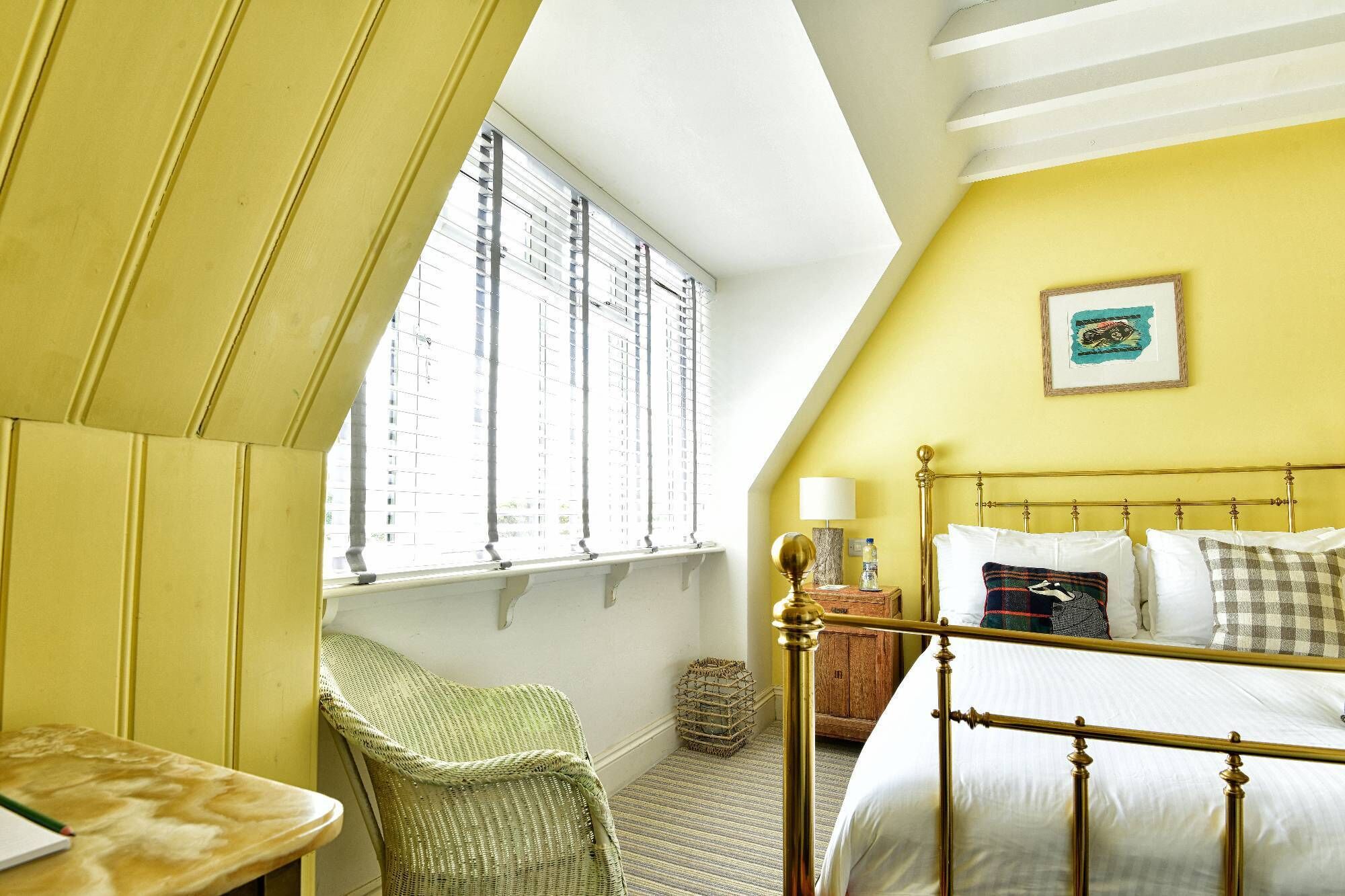 A bedroom with a bed, a chair, a bedside table, a lamp, and a window with blinds.