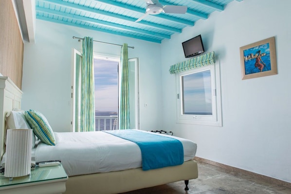 Un dormitorio con cama, televisor montado en la pared, ventana con vistas y ventilador de techo.