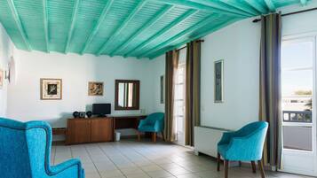 A living room with teal ceiling beams, a wooden desk, two blue chairs, and a large window with curtains.