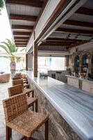 An outdoor bar area with a long counter, wicker chairs, and stone walls.