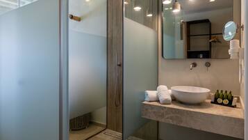 A modern bathroom with a glass shower enclosure, a large mirror, a white sink, and pendant lighting.