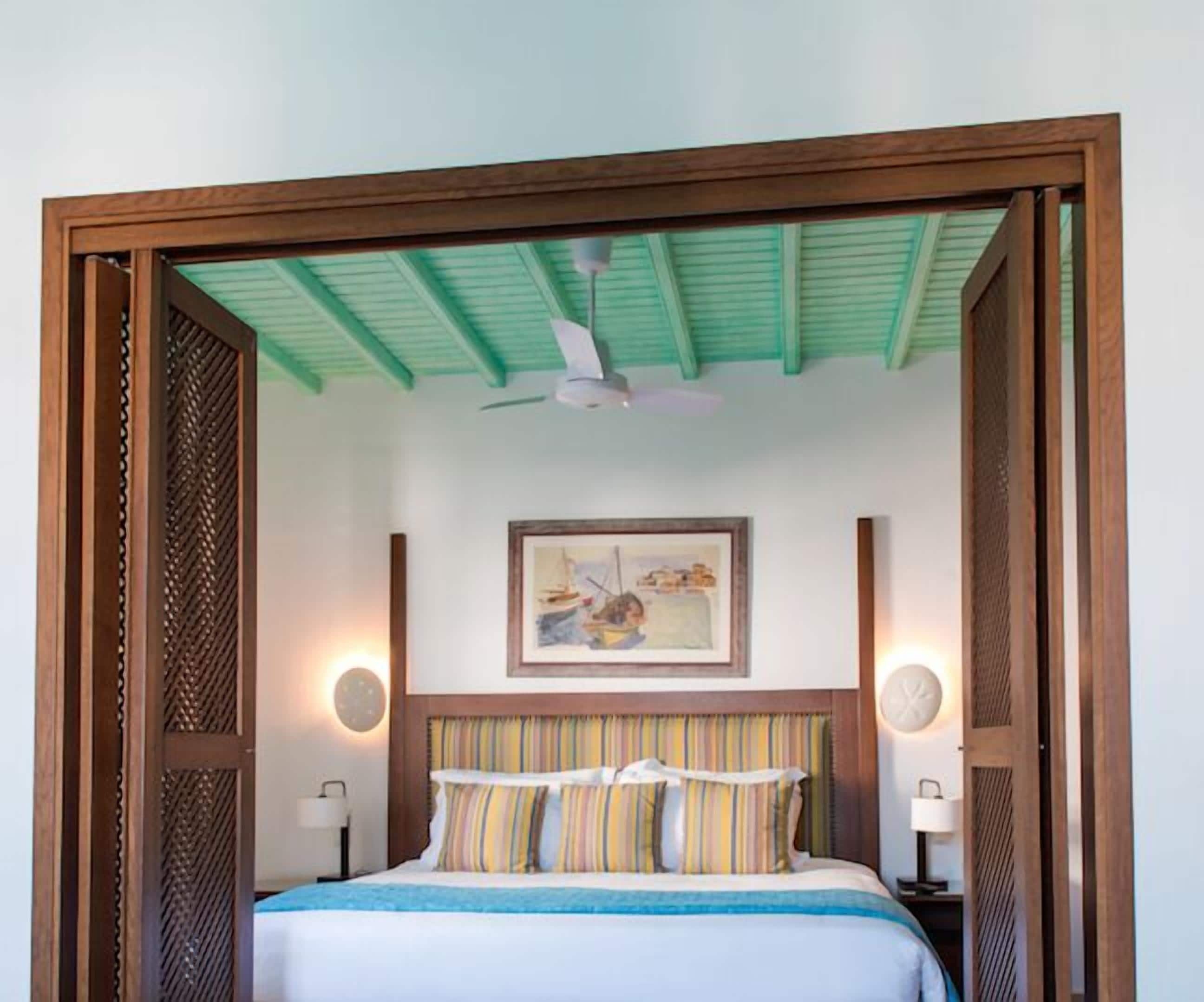 A bedroom with a bed, a ceiling fan, a painting, and two bedside lamps.