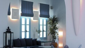 A modern living room with a sofa, a bench, a large potted plant, and a unique wall art piece. - Poseidon Hotel & Suites (Mykonos)