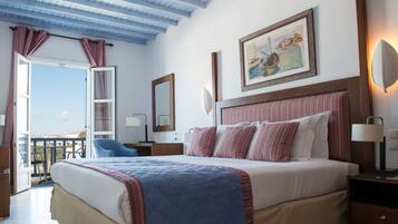 A bedroom with a large bed, a headboard with a striped pattern, a painting above the bed, a nightstand with a lamp, and a view of the outdoors through an open door.
