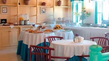 A dining area with round tables covered in white tablecloths, surrounded by red chairs. There are shelves with pottery and framed pictures on the wall.