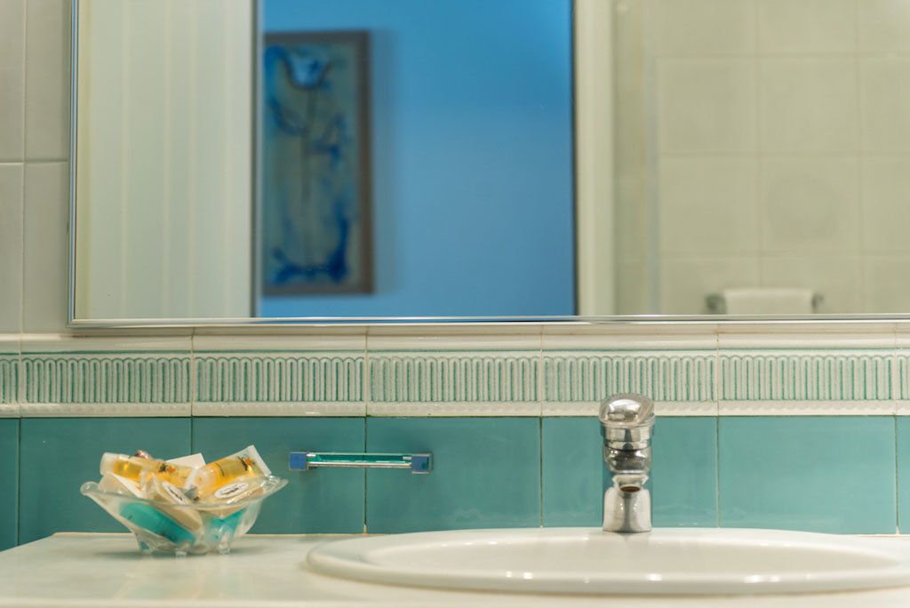 A bathroom with a white sink, a glass bowl with toiletries, and a mirror above the sink.