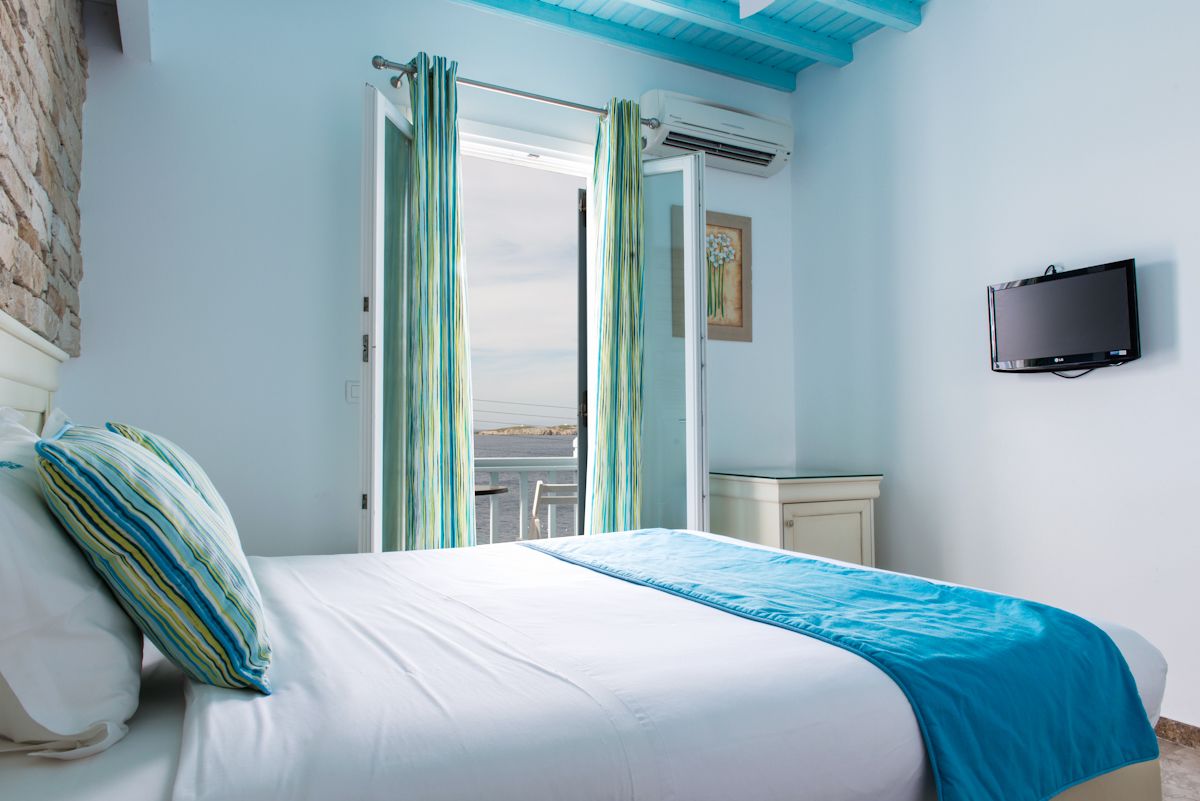A bedroom with a bed, a TV, and a view of the sea through an open door.