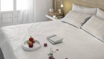 Una cama bien hecha con almohadas, una mesita de noche con lámpara y una bandeja con una bebida y pétalos de rosa.