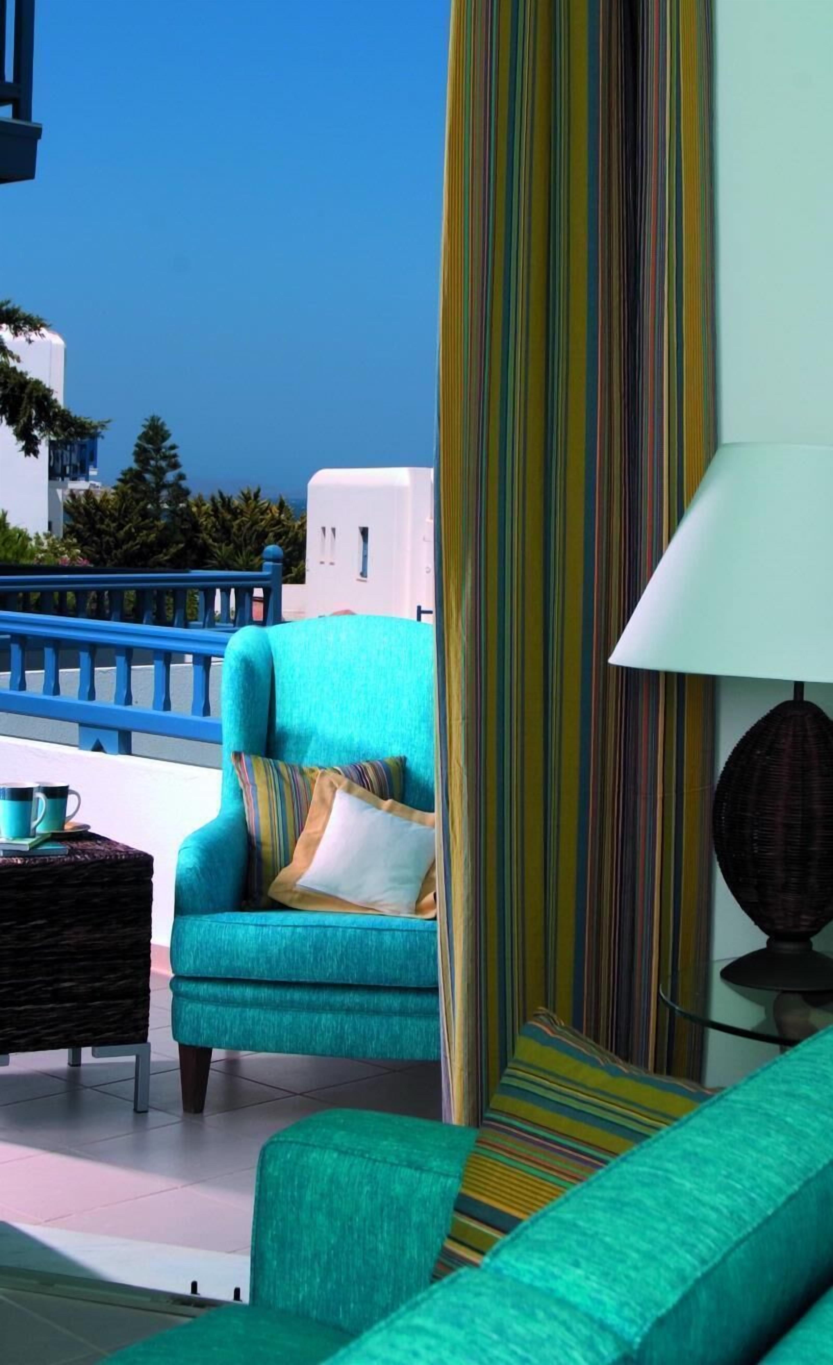 Un sillón azul verdoso con un cojín a rayas, una mesita de mimbre y una lámpara de pie.