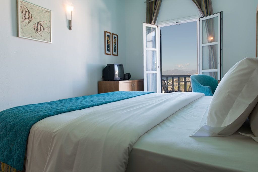 Ein Hotelzimmer mit einem Bett, einem Schreibtisch mit Computer, einem Fenster mit Vorhängen und Blick ins Freie.
