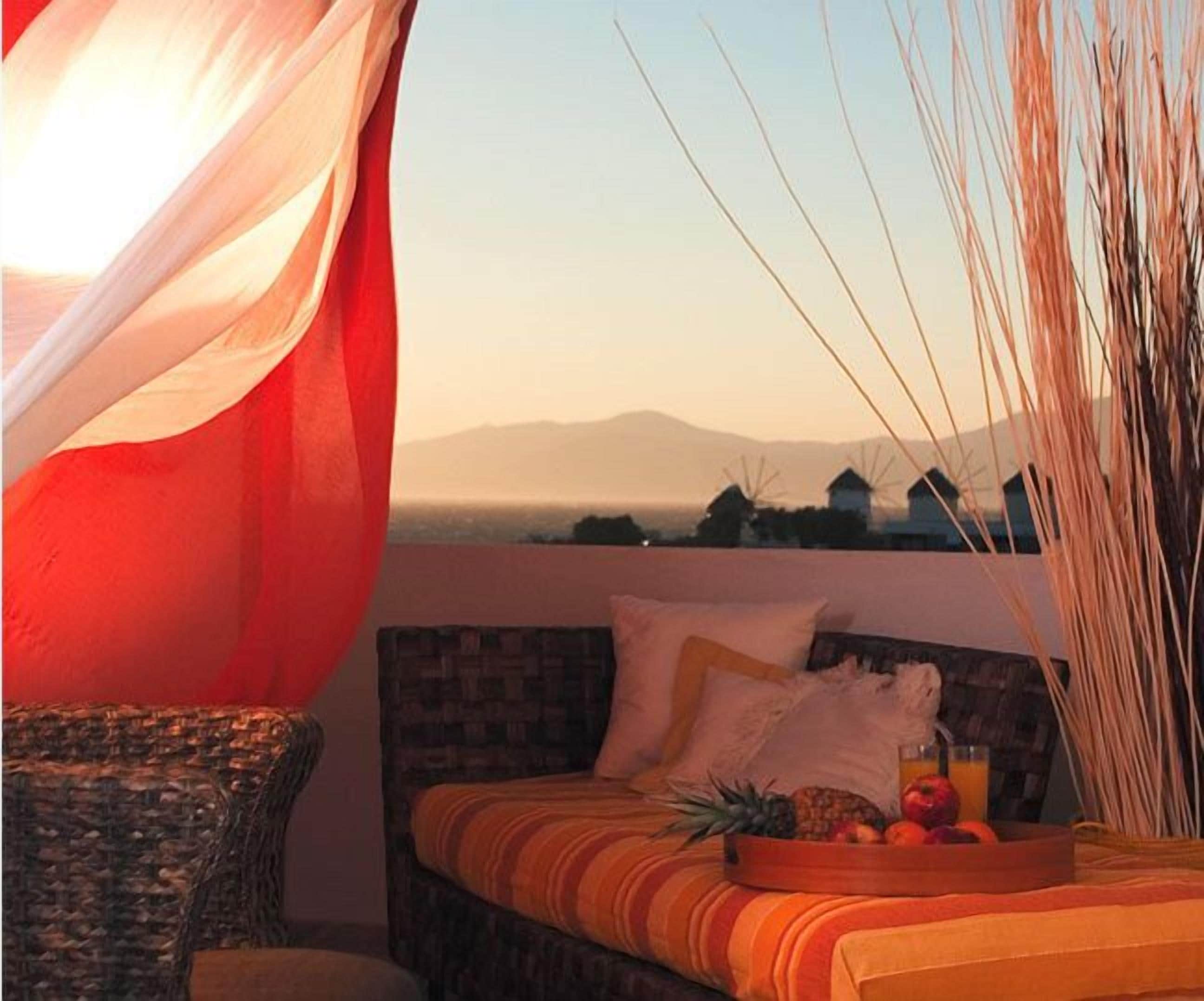 A bedroom with a bed, a wicker chair, and a view of windmills and mountains.