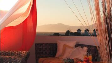 A bedroom with a bed, a wicker chair, and a view of windmills and mountains.