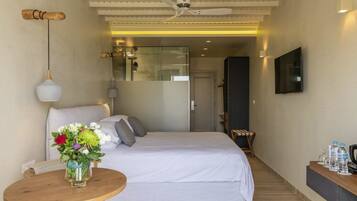 A hotel room with a bed, a round wooden table with a vase of flowers, a ceiling fan, and a TV mounted on the wall.