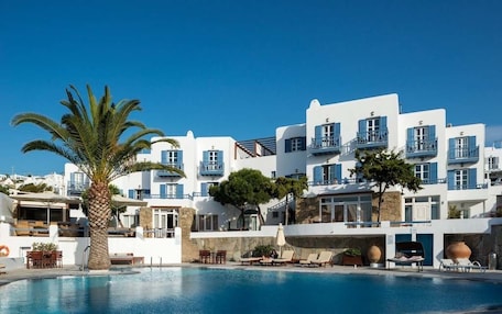 A poolside area with a clear blue sky, white buildings with blue shutters, and a palm tree.