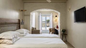 Une chambre d’hôtel avec un grand lit, un bureau avec une chaise, une télévision et une vue sur l’extérieur, visible à travers une porte en arc de cercle.