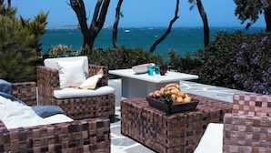 A coastal outdoor seating area with wicker furniture and a table with fruits and drinks. - Poseidon Hotel & Suites (Mykonos)
