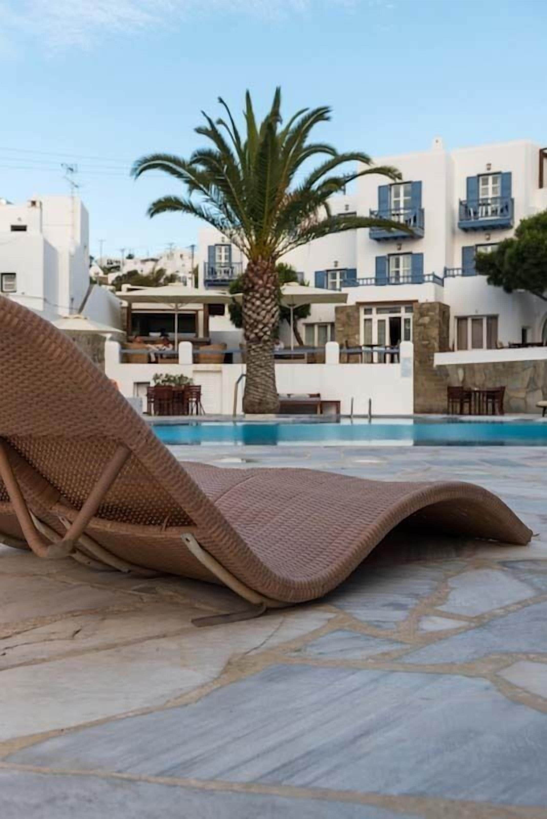 A poolside area with a lounge chair, a palm tree, and a building with balconies.