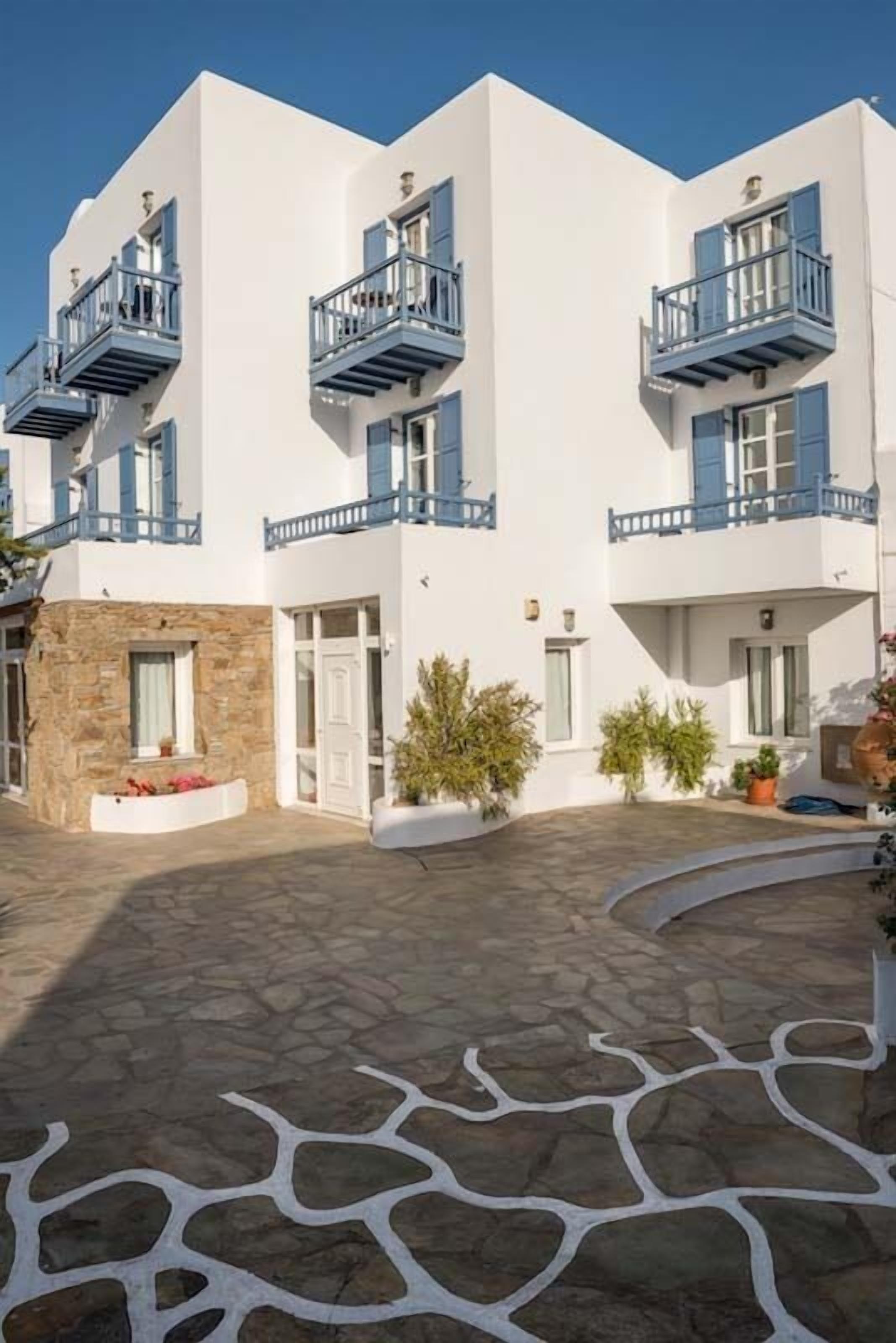 A white building with blue balconies, stone flooring, and potted plants.