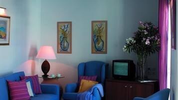 A living room with a blue sofa, armchairs, a small table with a lamp, and a television.