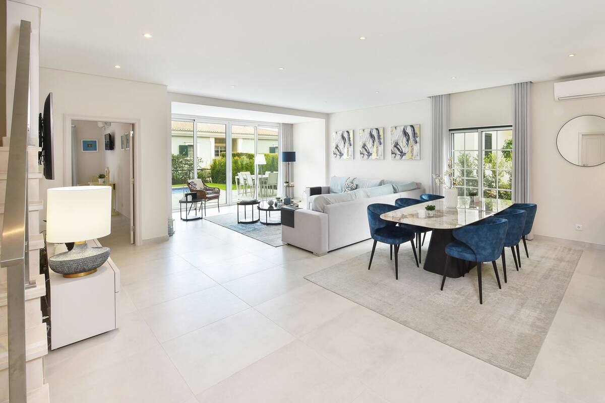A modern living room with a dining area, large windows, and a view of the outdoors.