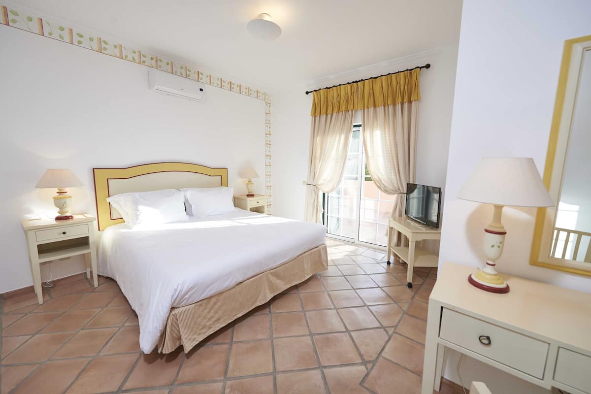 A hotel room with a bed, bedside tables with lamps, a TV, a desk, and a chair.