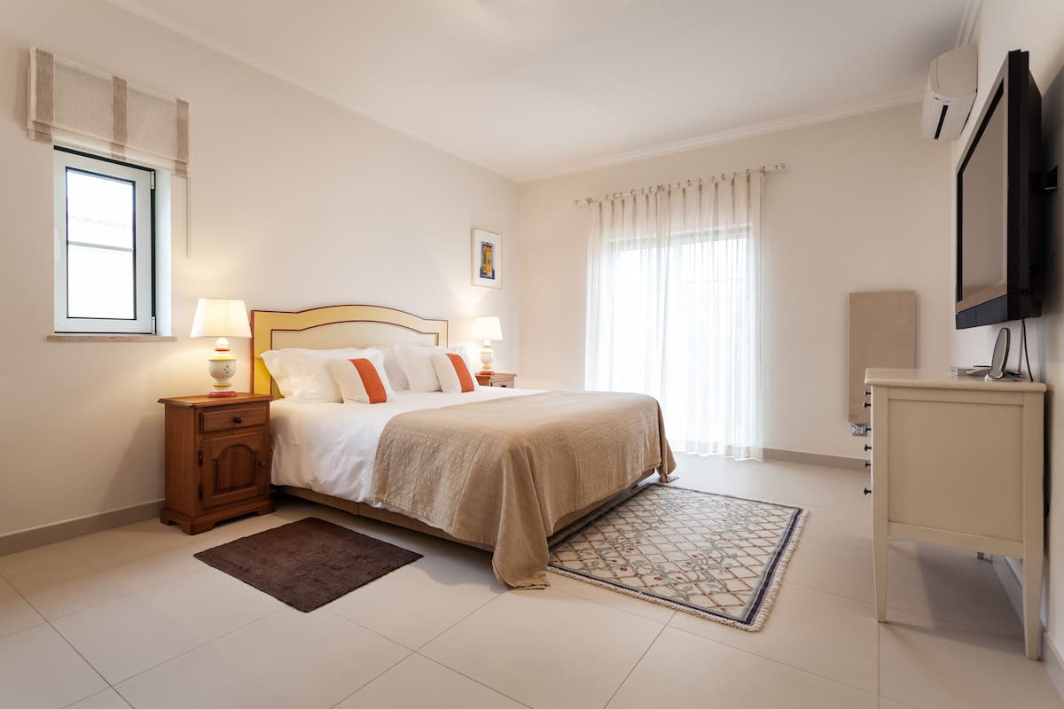 A hotel room with a bed, bedside tables, a TV, and a window with curtains.
