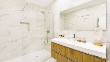A modern bathroom with a glass-enclosed shower, a white marble wall, a wooden vanity, and a large mirror.