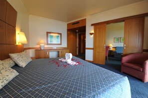 A hotel room with a large bed, a desk, a chair, and a wardrobe.