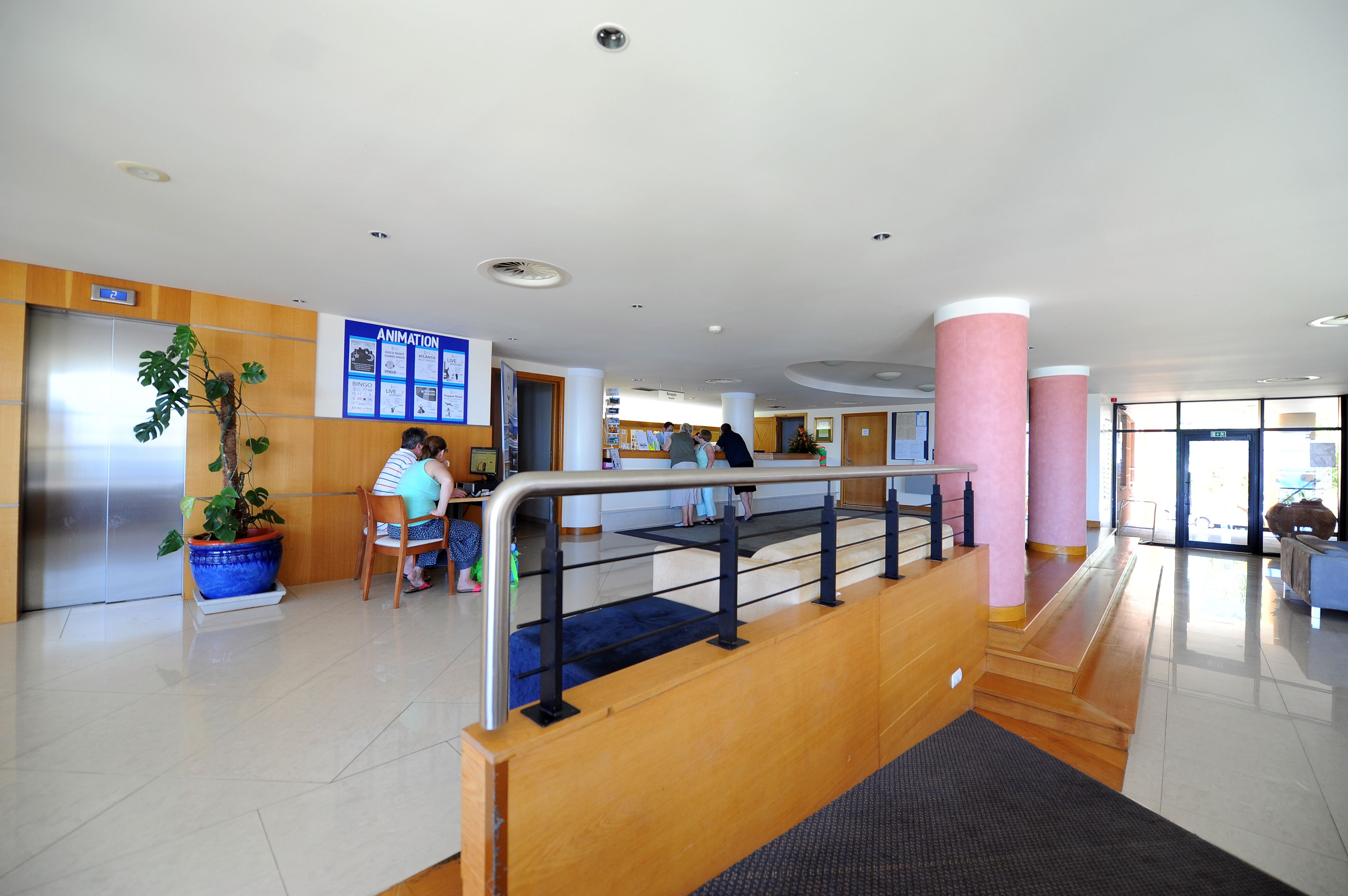 A modern lobby with a reception desk, a staircase, and a large potted plant.