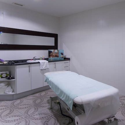 A clinical examination room with a bed, examination table, and a shelf with towels.