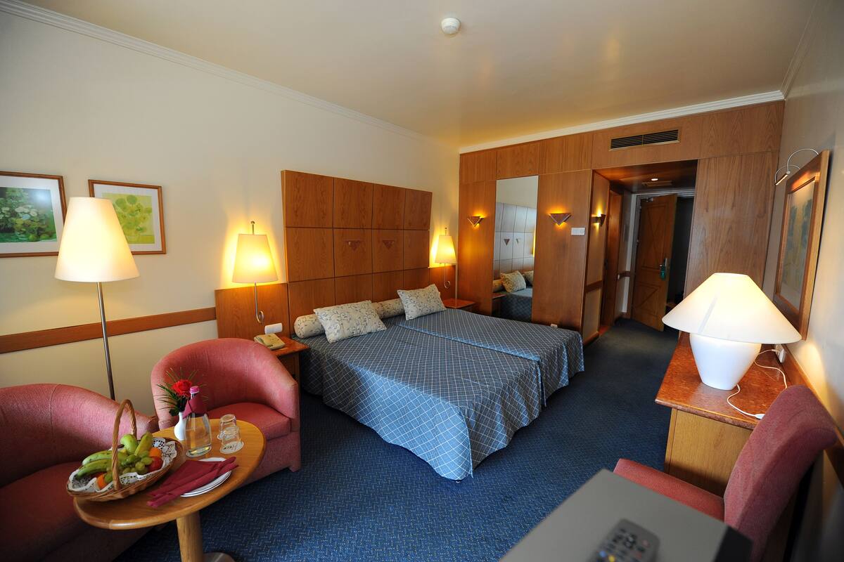 Une chambre d’hôtel avec un lit, deux fauteuils, une petite table sur laquelle se trouve un panier de fruits et une lampe.